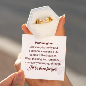 Close-up of golden butterfly ring with pink stone and gift card in a velvet box