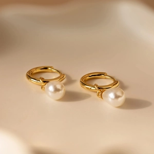 Elegant gold huggie earrings with teardrop freshwater pearls on a minimalist beige tray