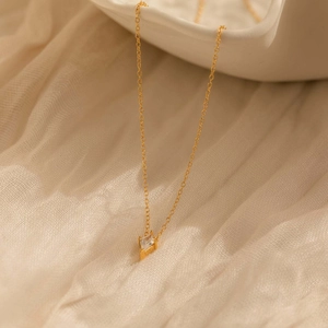 Detail shot of a minimalist gold geometric square zircon pendant on a soft beige fabric