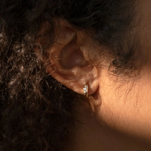 Elegant gold clover hoop earrings with marquise-cut zircons worn on model's ear
