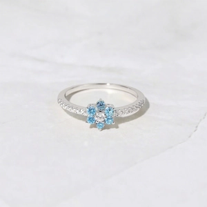 S925 sterling silver flower ring with blue zircons and center stone on marble background