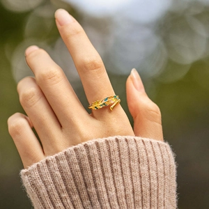 Bague feuille dorée avec émail coloré portée par un modèle sur fond flou doux