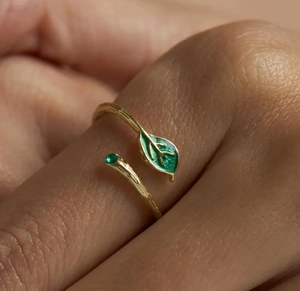 Detail of adjustable gold ring featuring green enamel leaves and a small gemstone