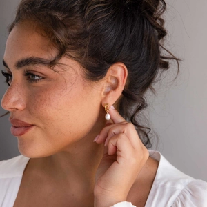 Close-up of golden letter E earring with irregular white pearl drop on model