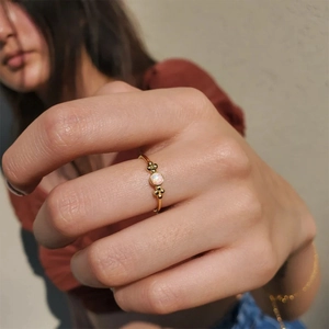 Elegant gold flower ring with round opal gemstone shown on a model's finger in soft lighting