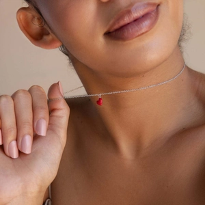 Détail du pendentif cœur en émail rouge sur une fine chaîne en argent portée par un mannequin