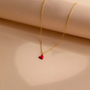 Détail du collier coeur doré en émail rouge projetant une ombre en forme de coeur