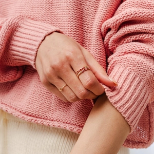 Close-up of minimalist gold ring set with red gemstones on a pink sweater background