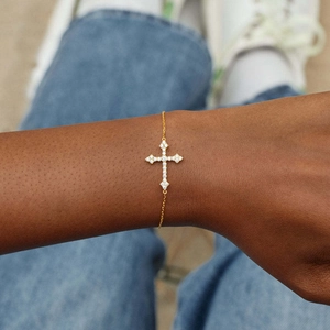 Gros plan d'un bracelet croix doré serti de zircons porté au poignet d'une femme