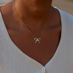 Gros plan d'un collier pendentif nœud doré avec zircons bleu clair porté par un mannequin