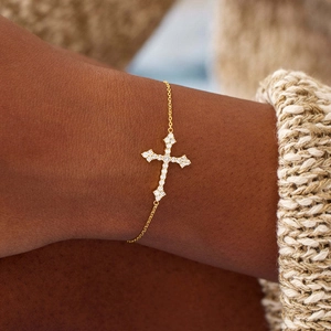 Gros plan d'un bracelet croix doré serti de diamants scintillants sur un poignet