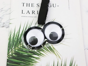 Detail of creative luggage tag with big googly eyes and black nylon strap on marble surface