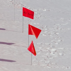 Red PVC marking flags on wire stakes with 'Go here' text for outdoor surveying in snow