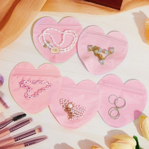 Pink heart-shaped matte PVC jewelry pouches with zip lock on white wooden background