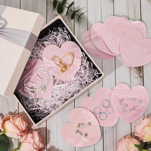 Pink heart-shaped PVC jewelry bag with a zip-lock closure and gold bracelet inside