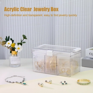 Three-compartment acrylic jewelry box showing stored earrings and golden bracelets