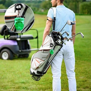 Green golf ball marker tool with metal hook attached to a golf bag in outdoor setting