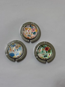 Set mit drei faltbaren Taschenhaltern aus Metall mit eleganten Blumenmustern auf grauem Grund
