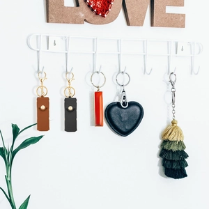 Detail showing various PU leather lipstick pouches and tassel keychains on a white wall hook