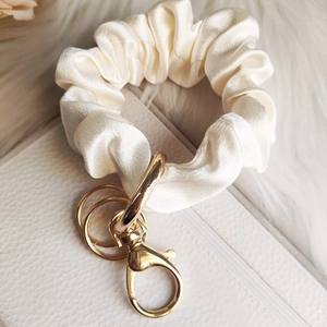 Detailed shot of cream satin scrunchie keychain with polished gold lobster clasp hardware