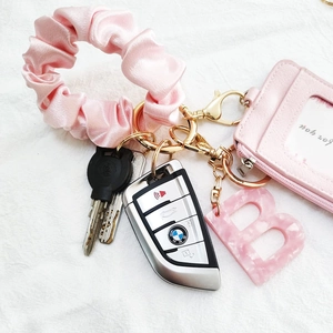 Close-up of pink satin scrunchie and leather card holder with gold metal keychain