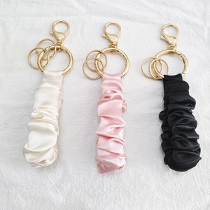 Detail of satin scrunchie keychains in white, pink, and black with gold metal hooks