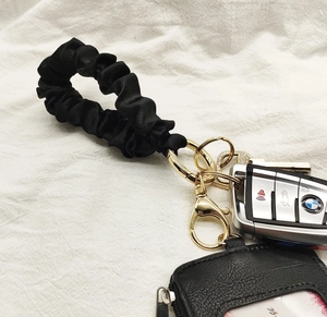 Close-up of black pleated wristlet keychain with golden ring and matching mini pouch