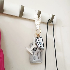 Close-up of white pleated satin wristlet with silver leather pouch and plane charm
