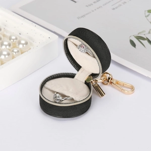 Detail of round black leather jewelry box with gold zipper and rings inside