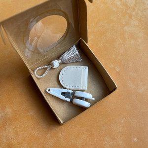 Detailed set featuring a white tassel, leather sheath, and clip in a kraft paper gift box
