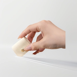 Hand holding minimalist beige suede jewelry pouch with gold snap button closure