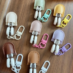 Mini precision scissors with colorful leather cases and matching snap hooks on wood