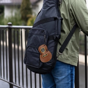 Guitar-shaped pick holder case in brown leather shown hanging on a guitar bag strap