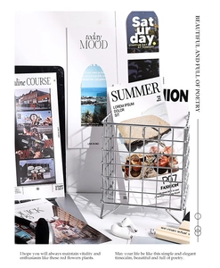 Panier de rangement en fil métallique argenté avec magazines et cartes sur bureau blanc