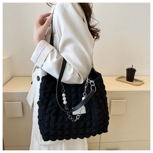 Black bubble texture tote bag with pearl and floral chain shown on a shoulder