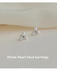 Detailed close-up of triple pearl cluster stud earrings on natural linen background