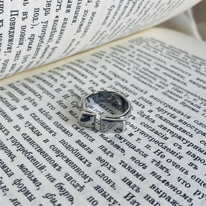 Close-up of silver open ring with irregular lava texture against a vintage book background
