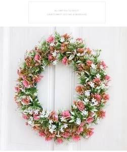 Dettaglio della ghirlanda di rose rosa e fiori bianchi appesa a una porta di legno bianca