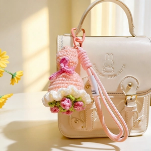 Handmade crochet pink doll flower bouquet keychain on a beige leather bag