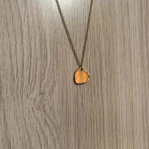 Macro detail of polished heart pendant in gold finish with delicate chain on wood
