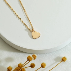 Gold heart pendant necklace for women with polished mirror finish on white pedestal