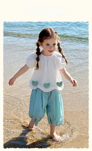 Detail of girl's summer set with white puff sleeve top and blue bloomers on a beach