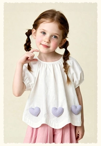 Detail of girls white cotton top with purple heart accents and pink pleated skirt