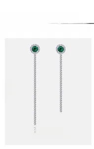 Macro detail of silver tassel earrings featuring a round green emerald and pave set stones
