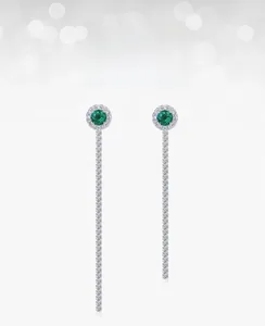Macro shot of long silver tassel earrings with round emerald gems and zircon stone pavé