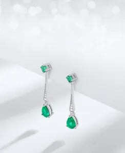 Close-up of teardrop emerald drop earrings with silver metal and small diamond accents