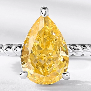 Pear cut yellow high carbon diamond ring with silver rope band on a textured background