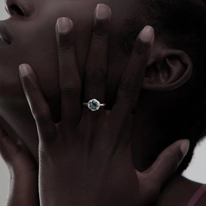 Close-up of rose gold ring with teal gemstone and diamond halo on model hand