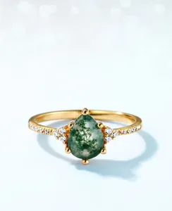 Close-up of teardrop moss agate ring with golden band and side diamond accents