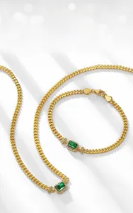 Makroaufnahme einer Gold-Panzerkette mit smaragdgrünem Stein und glitzerndem Besatz
